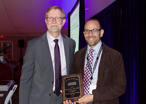 Two men posing for a picture, one accepting an award