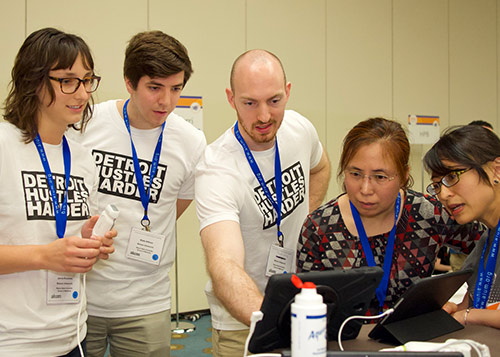 Five people standing in a semi circle looking at a video screen on a table