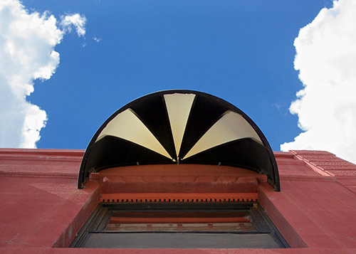 Looking up at a black and white circular awning with a white cloud and blue sky in the background